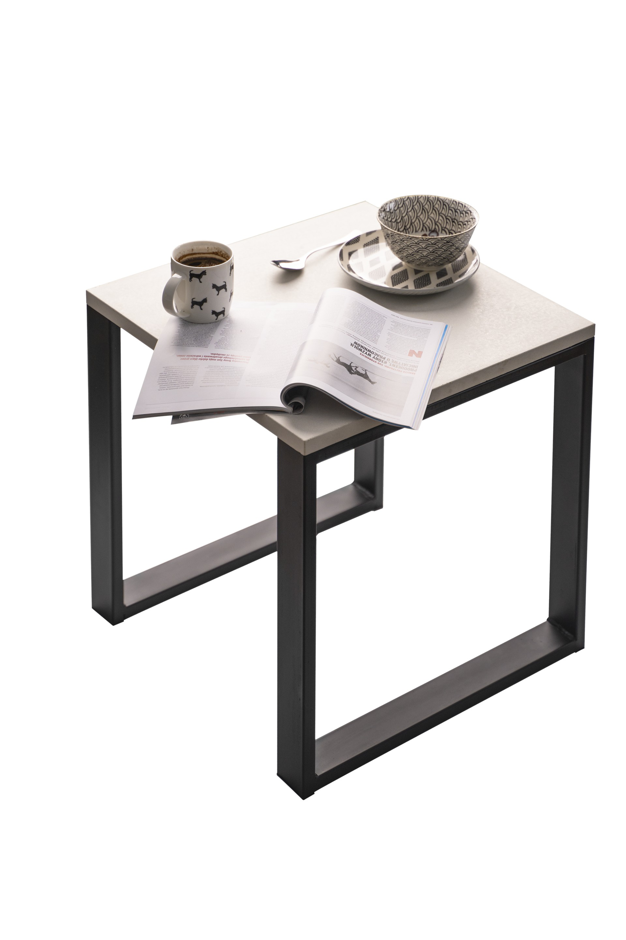 Stolik kawowy z blatem imitującym beton, czarną metalową podstawą, kubkiem z kawą, miseczką i otwartym magazynem.