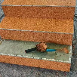 Schody pokryte żywicą epoksydową z kruszywem kwarcowym, widoczne narzędzia: kielnia i szpachelka, etap prac wykończeniowych.