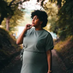 Portret kobiety w zielonej sukience, stojącej na leśnej ścieżce, zamyślona, z ręką pod brodą, spoglądająca w górę w lewo.