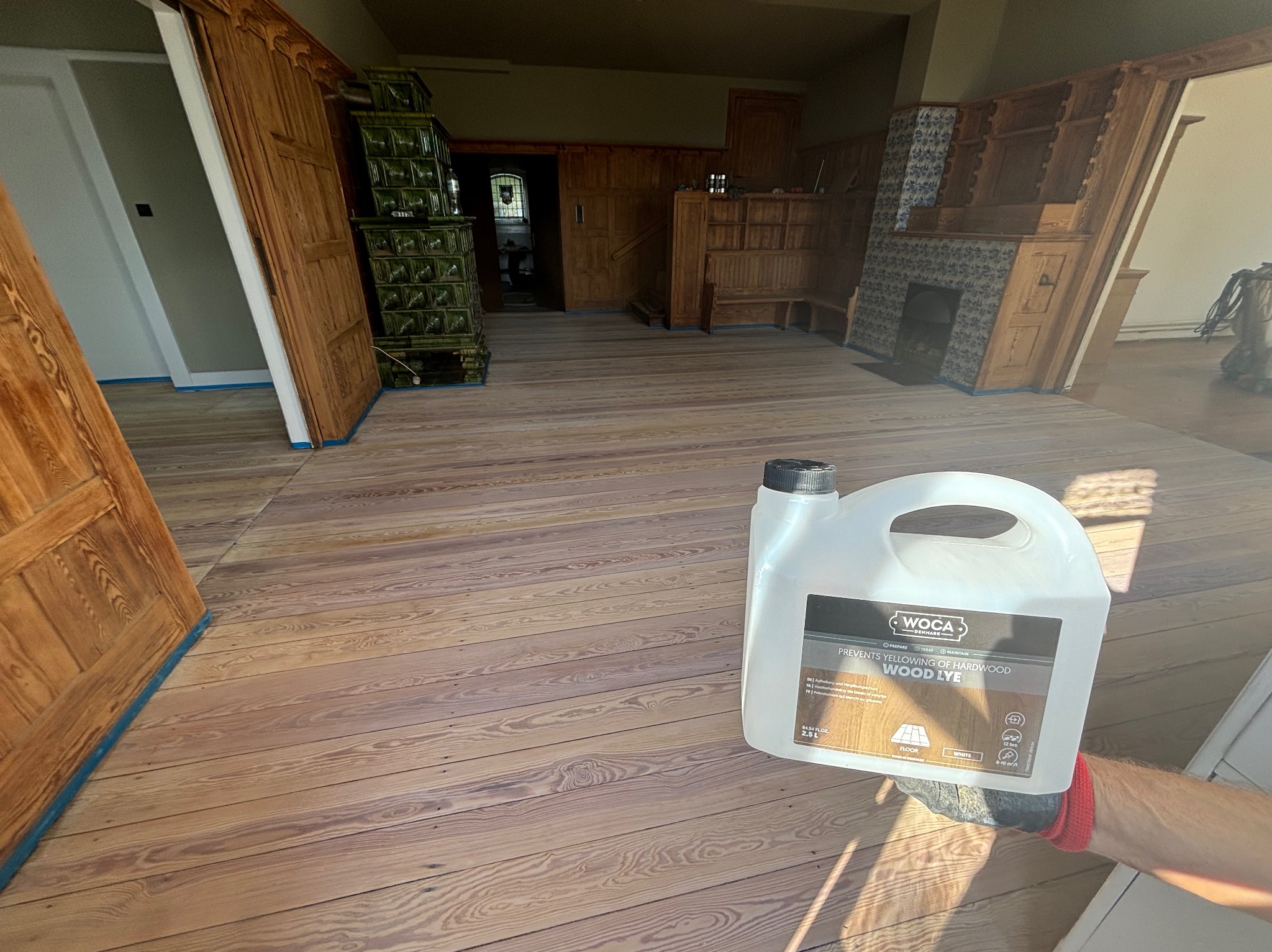 Poddasze po nałożeniu ługu do drewna WOCA, widoczne drewniane podłogi, drzwi i piece kaflowe, zabezpieczone taśmą malarską.