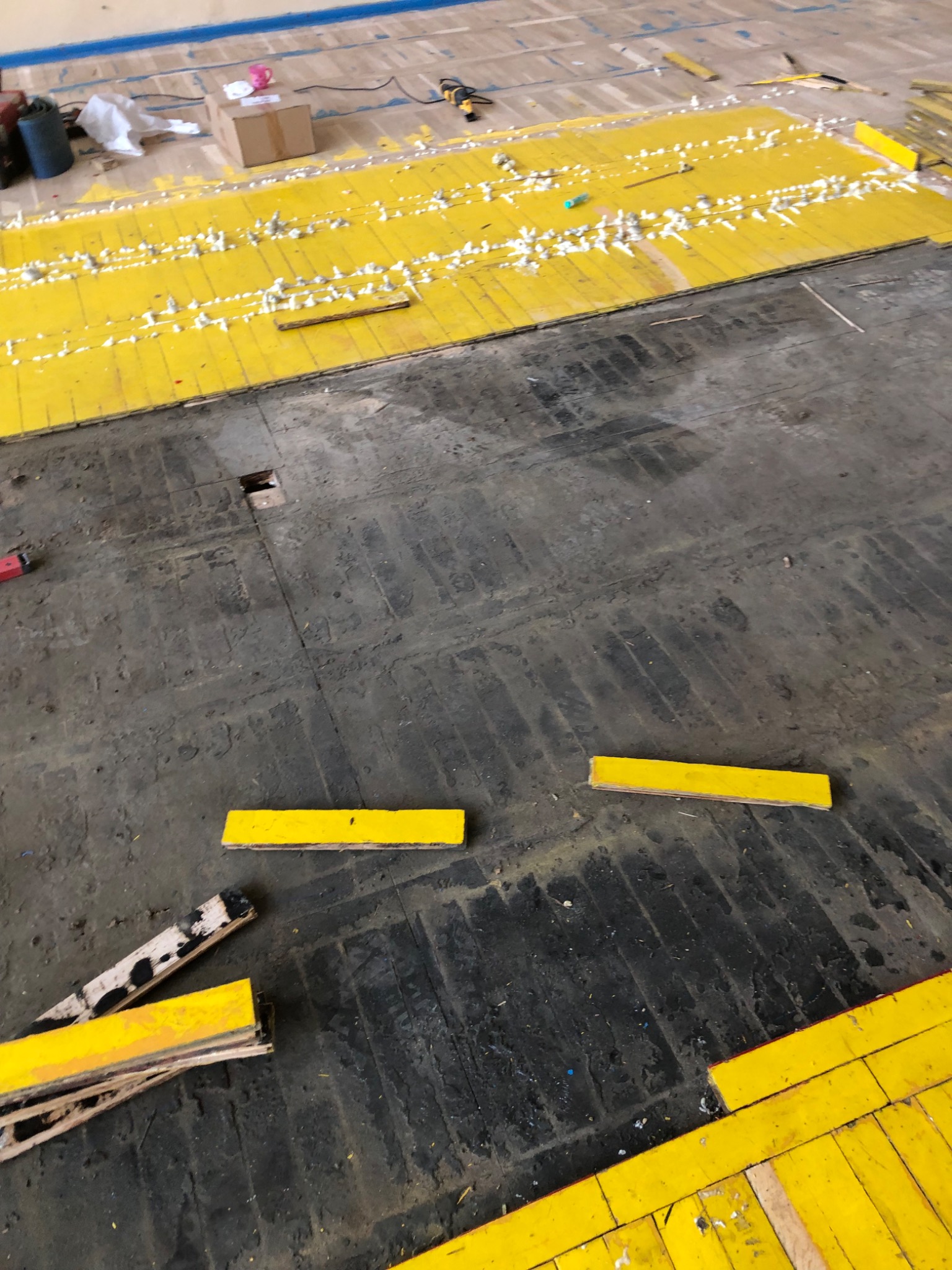Fragment podłogi z częściowo ułożonymi, żółtymi panelami parkietowymi, widoczne ślady starej podłogi w ciemnym kolorze i biała pianka montażowa między panelami.