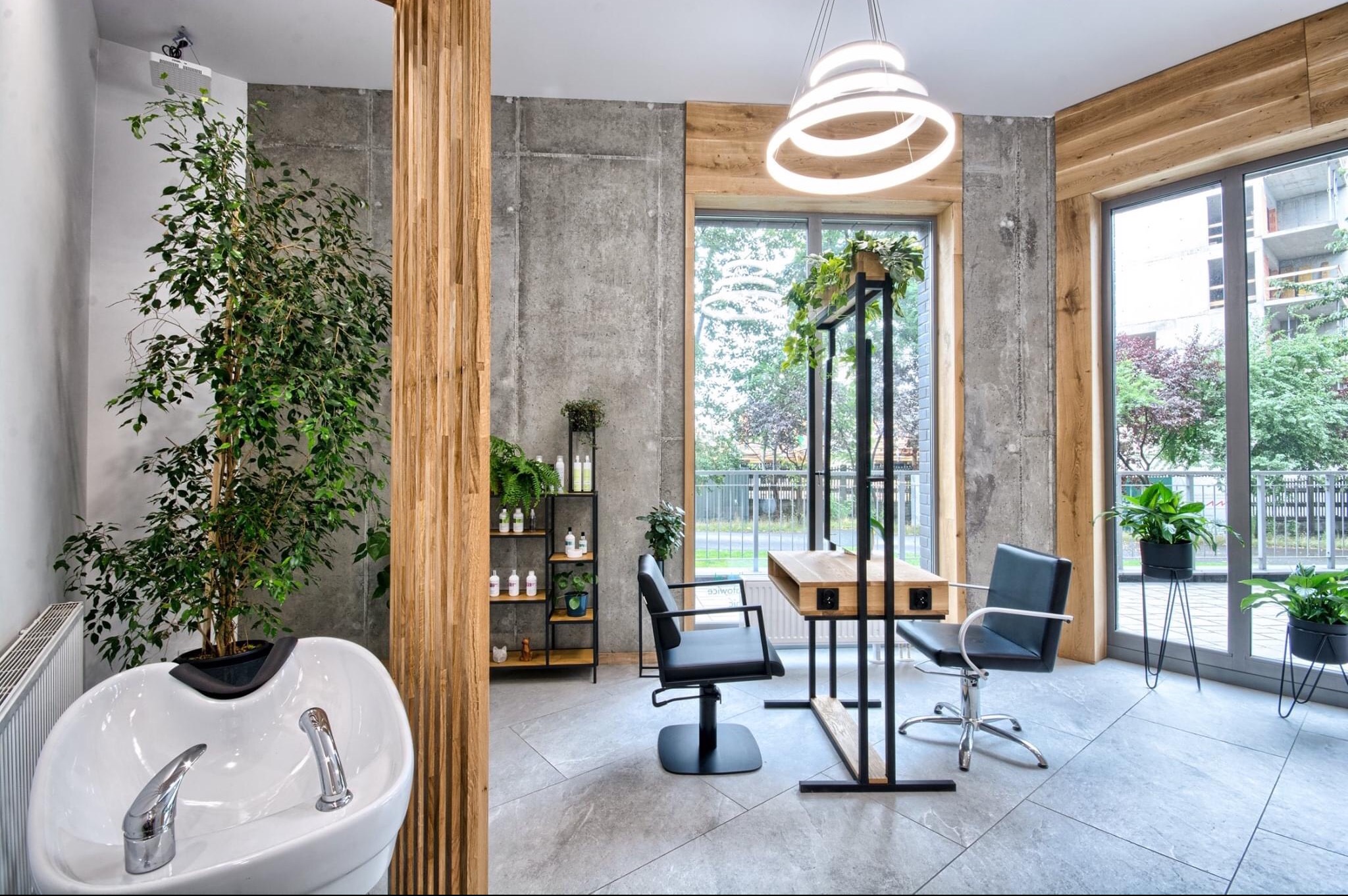 Nowoczesne wnętrze salonu fryzjerskiego z betonowymi ścianami, drewnianymi akcentami, stanowiskiem do mycia włosów i minimalistycznym oświetleniem.