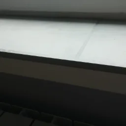 Szare panele podłogowe ułożone pod oknem, widoczne fragmenty grzejnika, słabe oświetlenie.