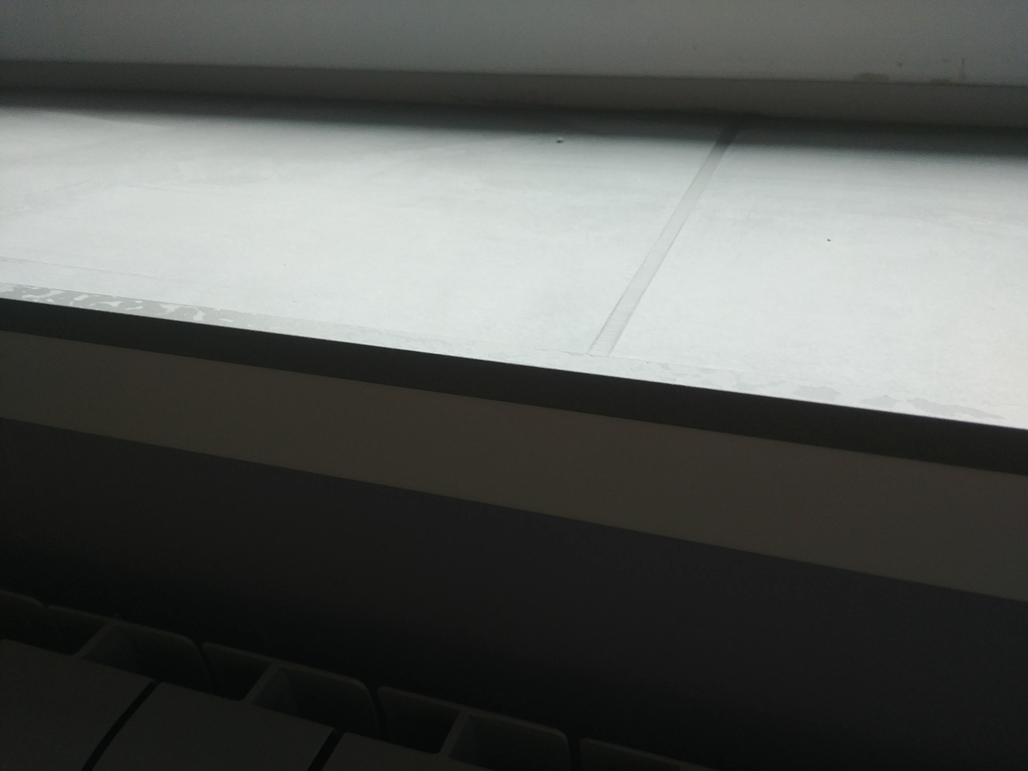 Szare panele podłogowe ułożone pod oknem, widoczne fragmenty grzejnika, słabe oświetlenie.