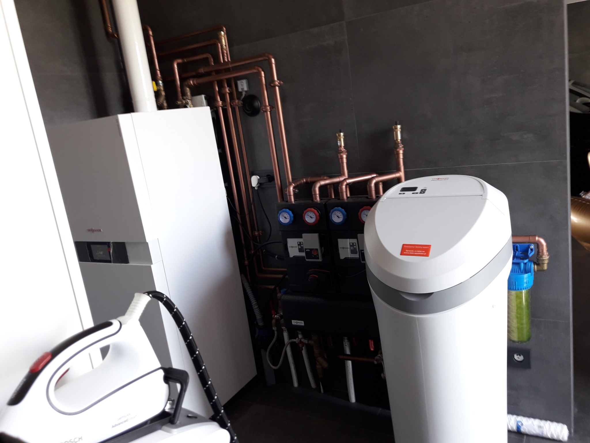 Nowoczesna kotłownia z piecem gazowym, systemem rur miedzianych, filtrem wody i stacją uzdatniania, a w tle żelazko parowe.