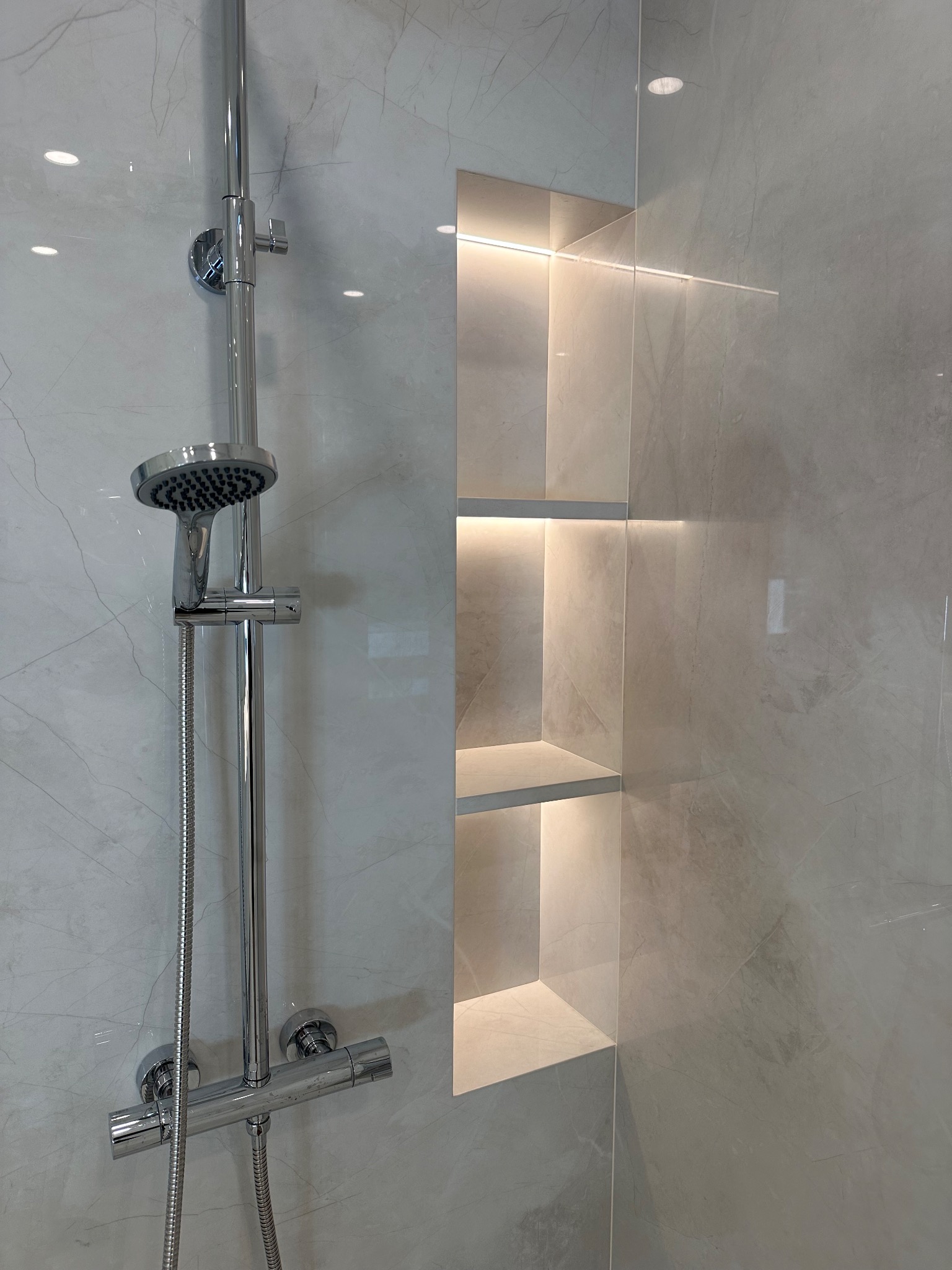 Wykończona łazienka: chromowana bateria prysznicowa na tle marmurowej ściany z wnęką oświetloną ledami. Minimalistyczny design, nowoczesne wykończenie.
