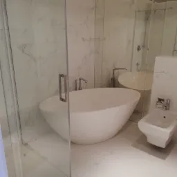 Nowoczesna łazienka z wolnostojącą wanną, szklaną kabiną prysznicową i bidetem, wykończona białym marmurem.