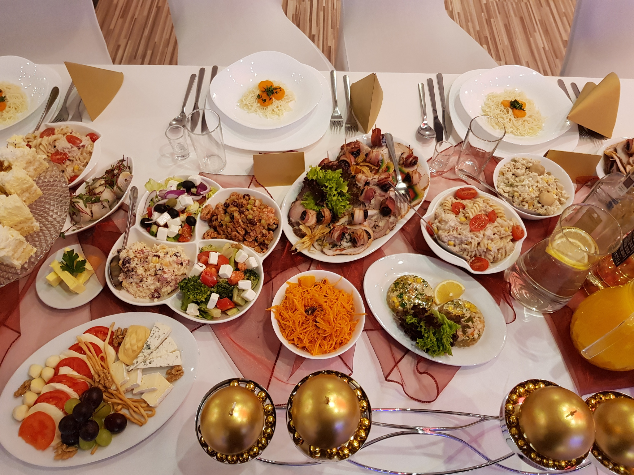Uroczysty stół cateringowy z różnorodnymi sałatkami, przekąskami i napojami, udekorowany złotymi świecznikami kulistymi, widok z góry.