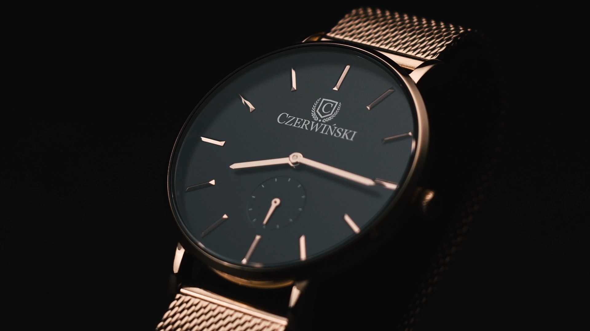 Elegancki zegarek marki Czerwiński z czarną tarczą, złotymi wskazówkami i bransoletą typu mesh, sfotografowany w zbliżeniu na ciemnym tle.