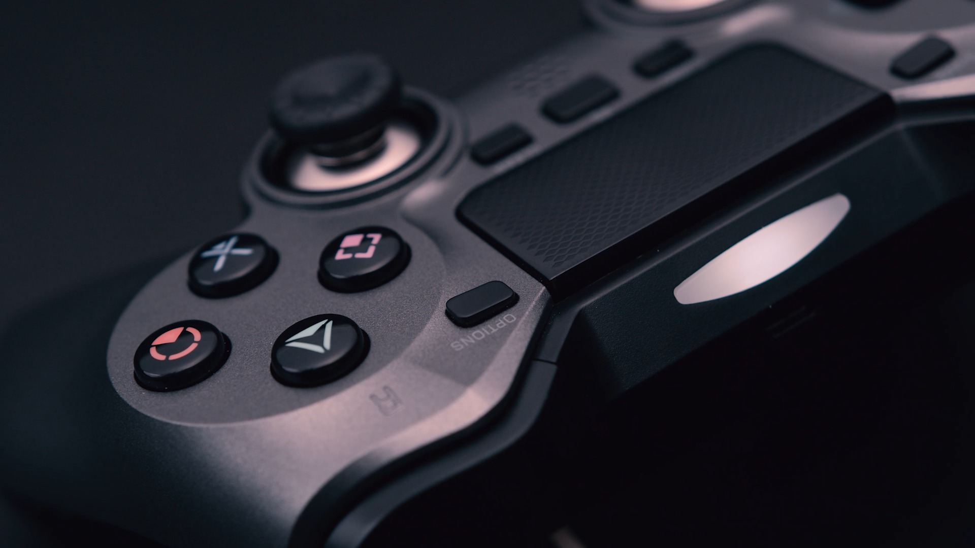 Szczegółowe ujęcie szarego kontrolera do gier z czarnymi przyciskami akcji i analogiem, oświetlonego z boku, na ciemnym tle.