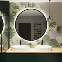 Nowoczesna łazienka z dwoma okrągłymi umywalkami, podświetlanym lustrem i heksagonalnymi płytkami z motywem roślinnym, oświetlona wiszącą lampą z żarówką Edisona.