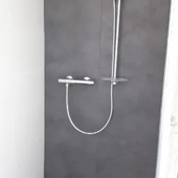 Nowoczesna kabina prysznicowa z ciemnoszarą płytką na ścianie i podłodze, biała płytka na bocznej ścianie, minimalistyczny zestaw natryskowy z termostatem.