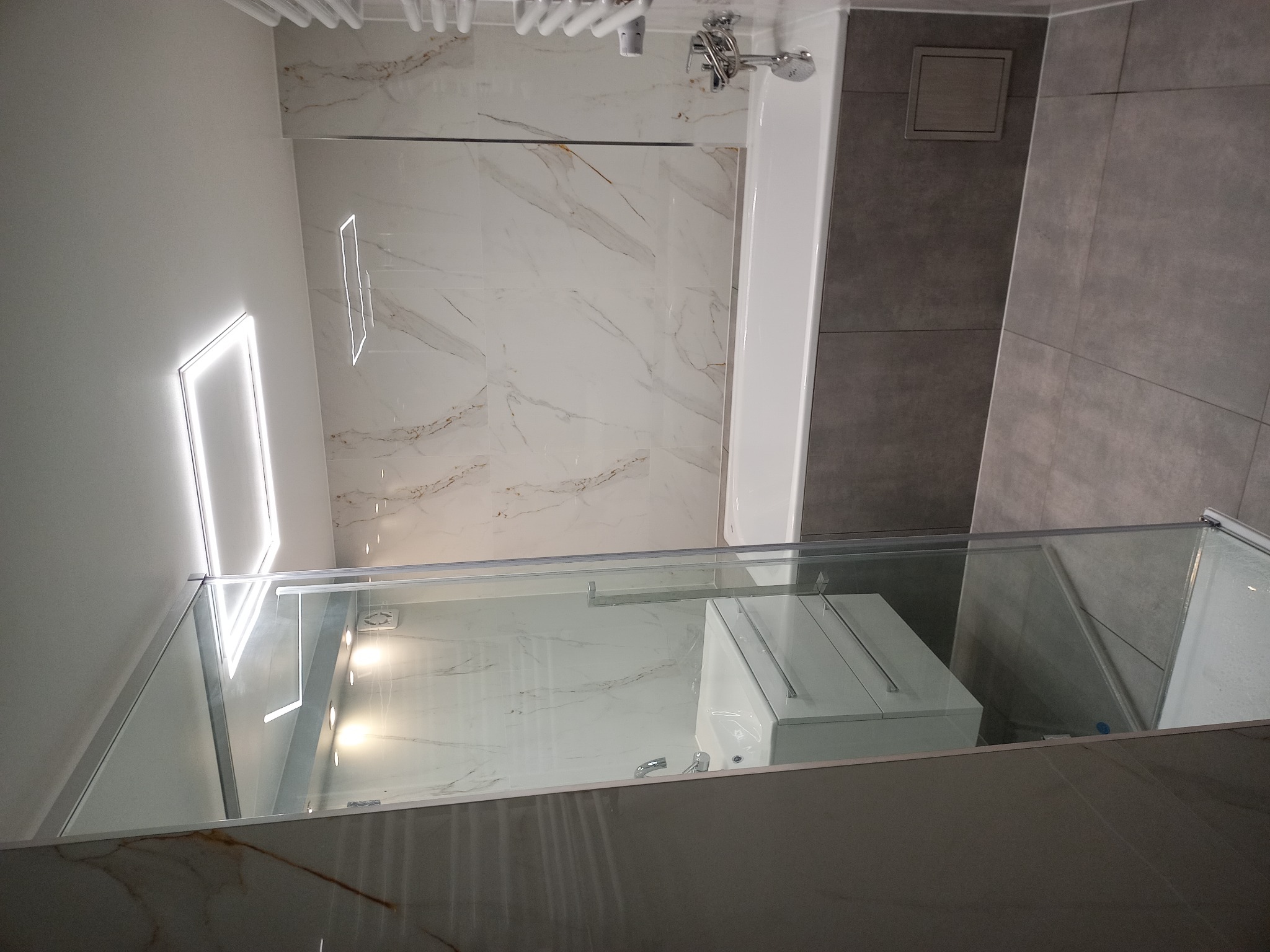 Nowoczesna łazienka z kabiną prysznicową typu walk-in, marmurowymi płytkami i podświetlanym lustrem, widok z góry.