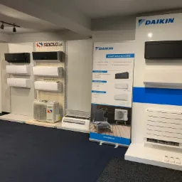 Ekspozycja klimatyzatorów marek Daikin i Sinclair w salonie, prezentacja różnych modeli na ścianach i postumentach, ulotka reklamowa Daikin widoczna w tle.