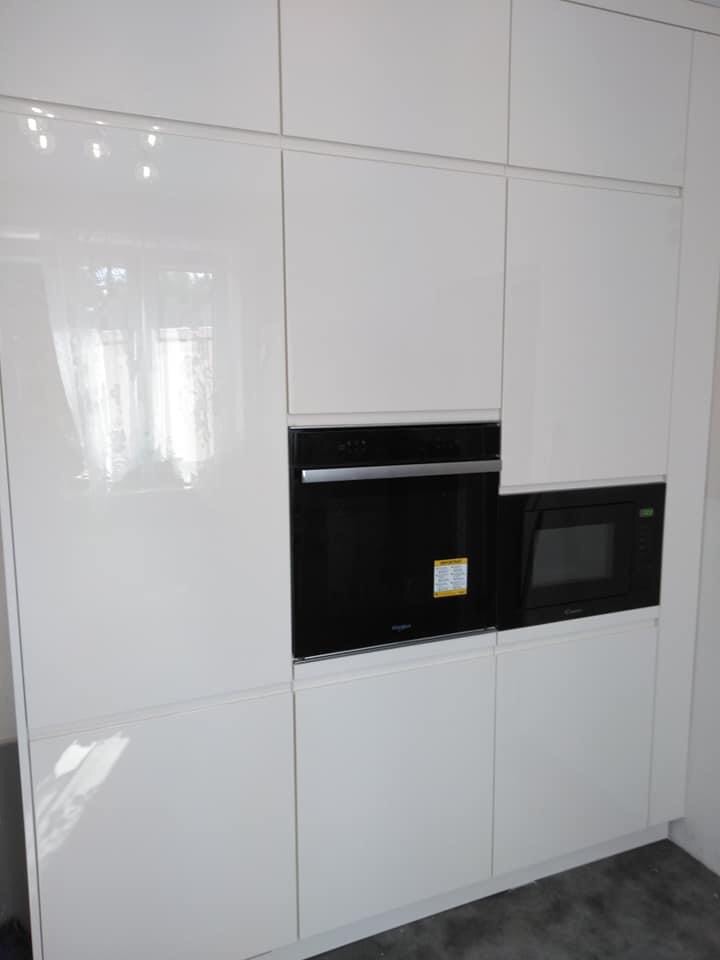 Biała, lakierowana zabudowa kuchenna z wbudowanym piekarnikiem i mikrofalówką, widok z dołu.