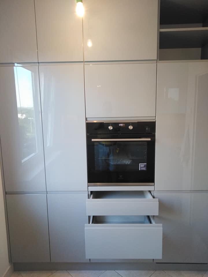 Biała zabudowa kuchenna z piekarnikiem i otwartymi szufladami, fronty na wysoki połysk.
