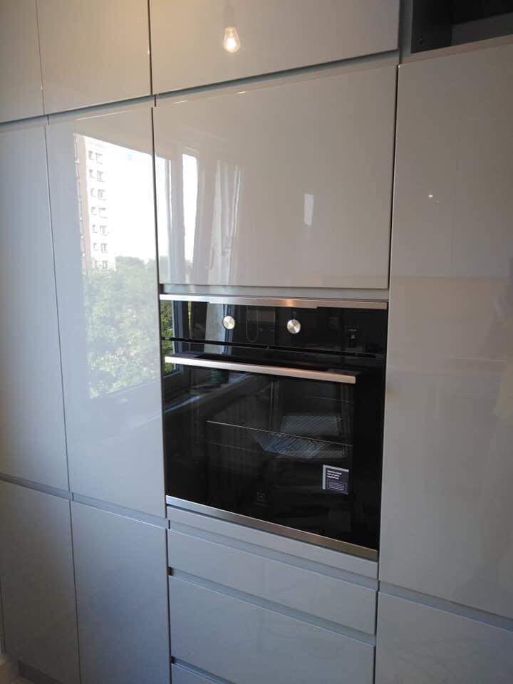 Szare, lakierowane szafki kuchenne z wbudowanym piekarnikiem elektrycznym, widok z bliska na połyskujące fronty i subtelne odbicia światła.