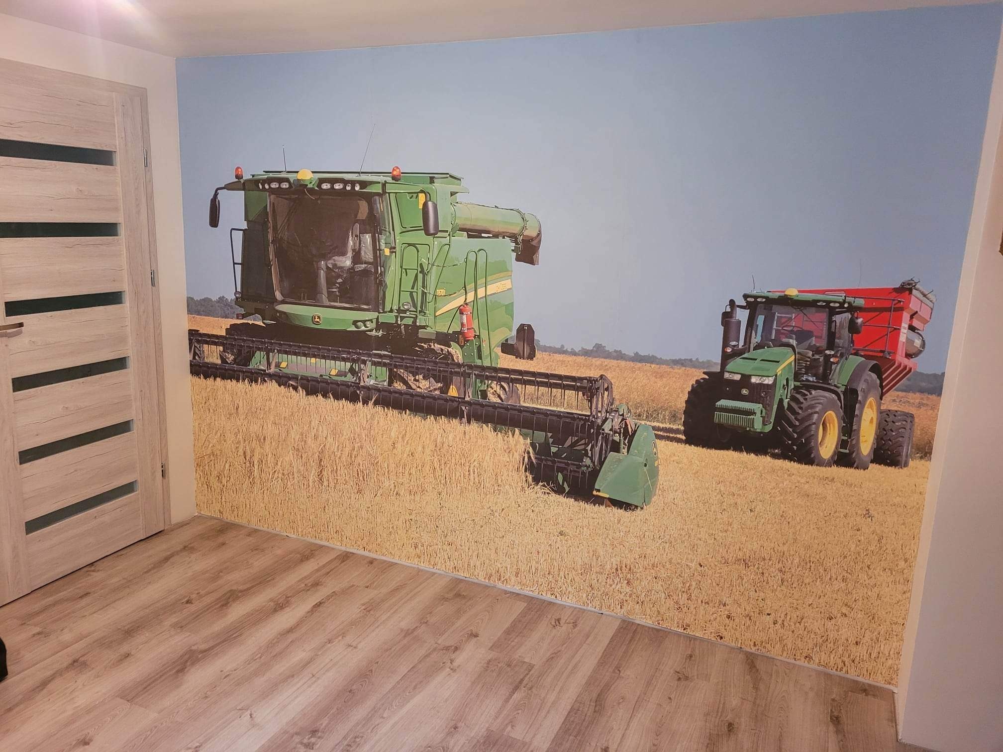 Fototapeta w pokoju przedstawiająca kombajn i traktor na polu zboża, widoczne z perspektywy podłogi z paneli i drzwi z przeszkleniami.