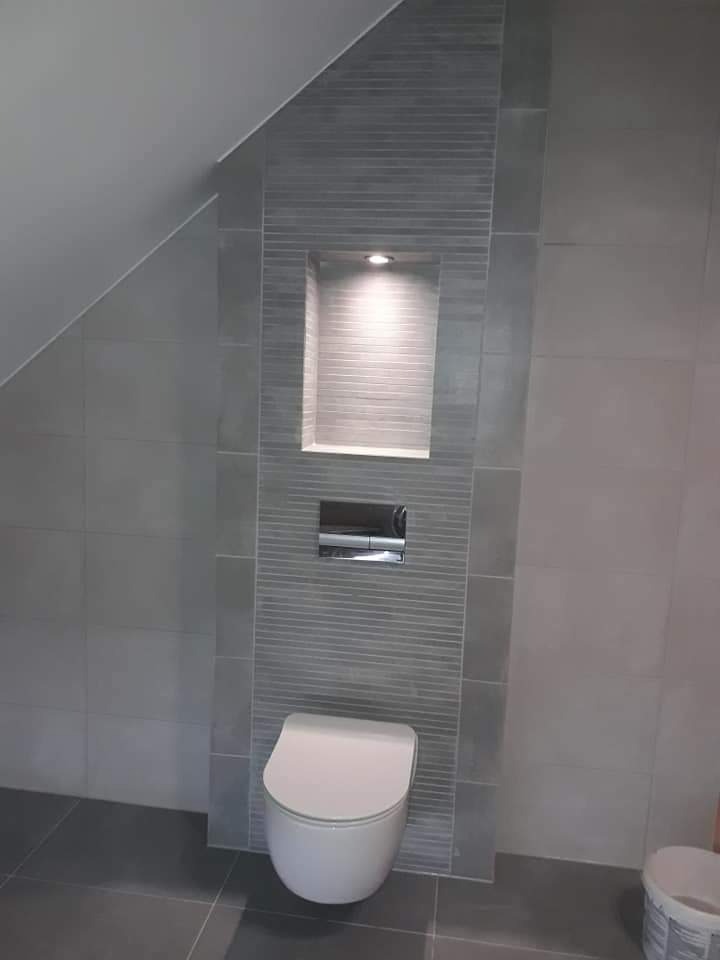 Szara łazienka na poddaszu z wiszącą toaletą i podświetlaną wnęką w płytkach