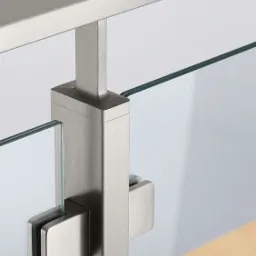 Szczegół mocowania szkła w balustradzie ze stali nierdzewnej, widoczne uchwyty zaciskowe i krawędź tafli szkła.