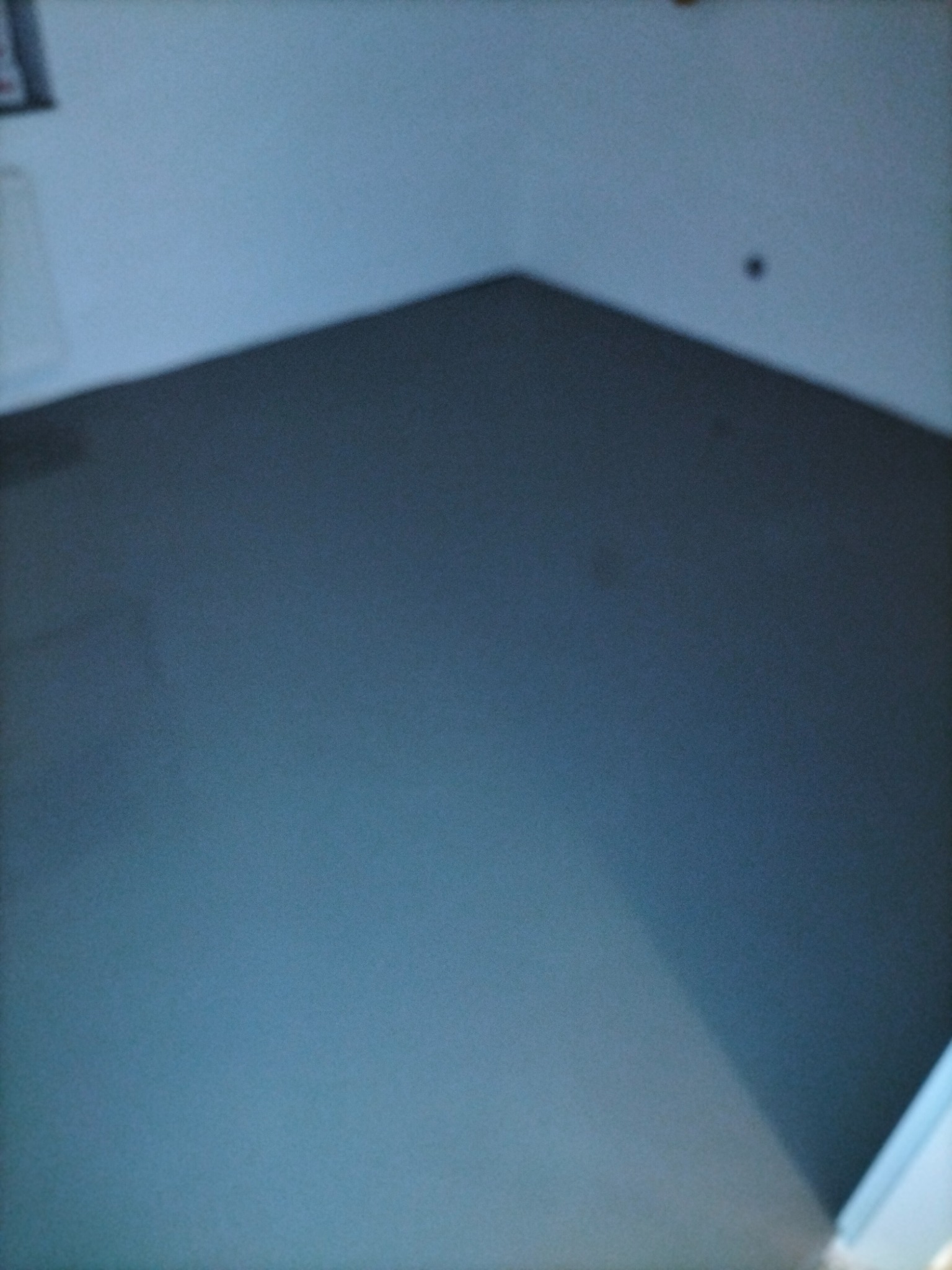 Gładka, szara posadzka w rogu pomieszczenia, widoczne połączenie ze ścianą, słabe oświetlenie.