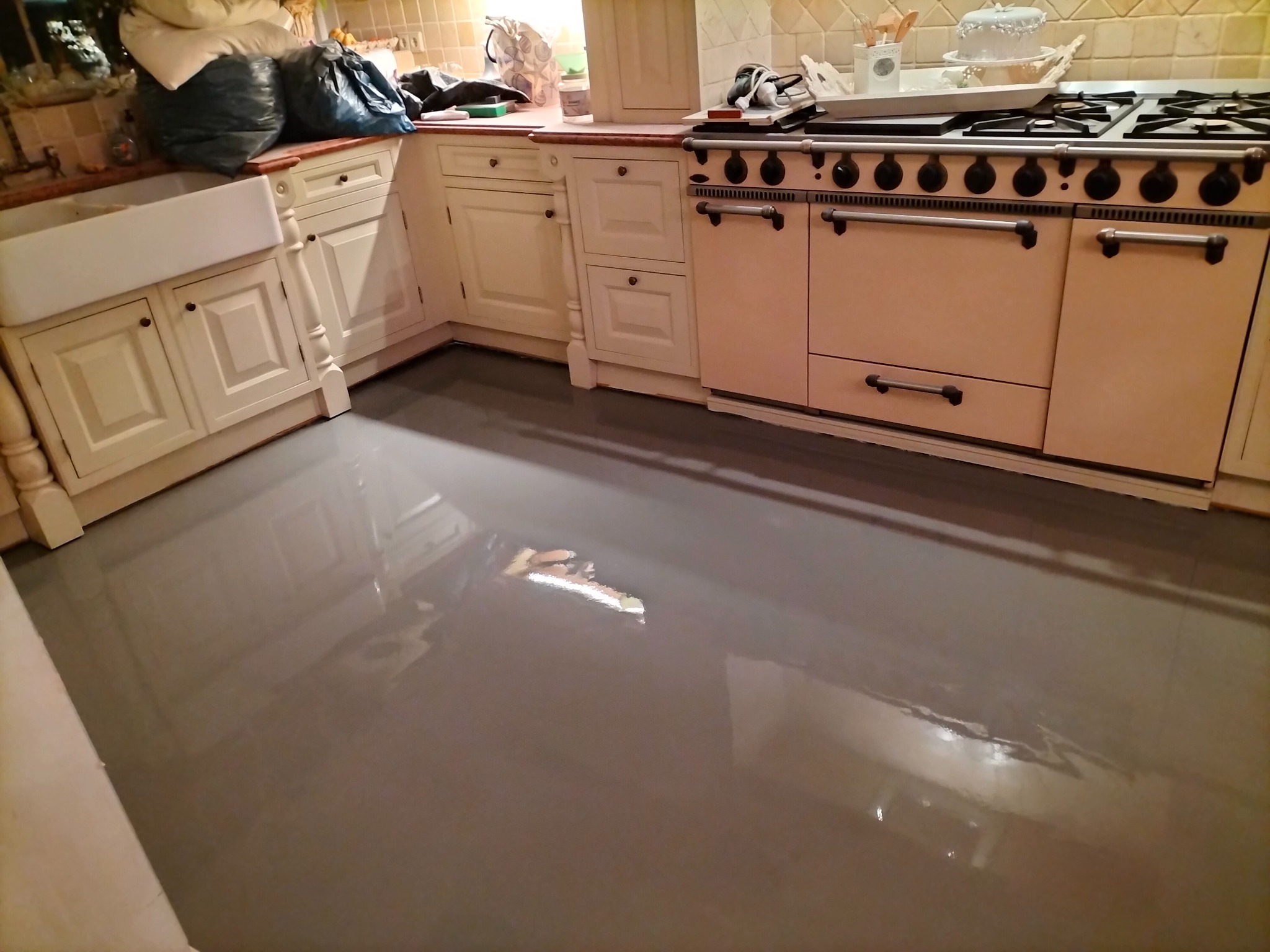 Świeżo wylana, gładka, szara posadzka w kuchni z beżowymi szafkami i dużą kuchenką gazową, widoczne delikatne refleksy świetlne.