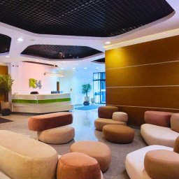 ZABŁYSZCZ Damian Błyszcz - Nowoczesne lobby biurowca z tapicerowanymi pufami w odcieniach beżu i brązu, recepcją z logo R4 i roślinami w donicach.