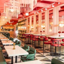 ZABŁYSZCZ Damian Błyszcz - Wnętrze restauracji w Opolu z długą, zieloną tapicerowaną ławą, czerwonymi krzesłami barowymi i białymi stolikami, oświetlone dekoracyjnymi lampami i wiszącymi instalacjami.