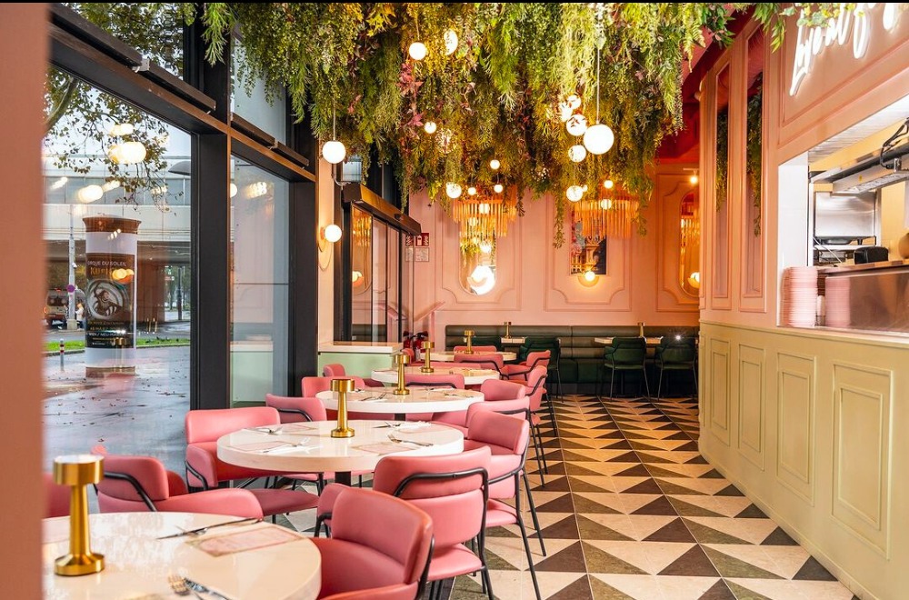 Wnętrze restauracji EL&N London Wiedeń z różowymi krzesłami, marmurowymi stolikami, roślinami zwisającymi z sufitu i geometryczną podłogą.