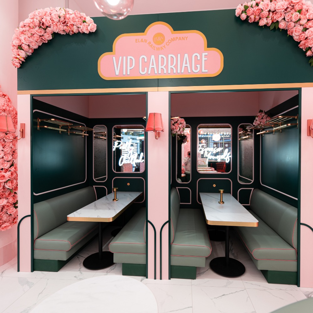 Różowo-zielone, tapicerowane loże w stylu wagonu VIP z marmurowymi stolikami i neonowymi napisami w lustrach, udekorowane kwiatami.