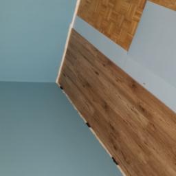 Stanisław Napierała - Fragment wnętrza z parkietem, panelami ściennymi imitującymi drewno i pomalowaną na niebiesko ścianą, widoczne pod kątem.