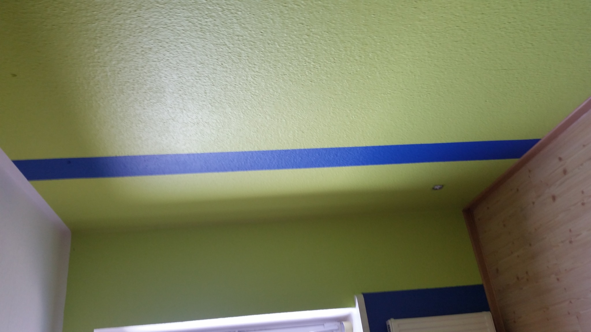 Ściana i sufit pomalowane na zielono z poziomym, niebieskim pasem dekoracyjnym w Żninie. Widoczny fragment ściany wyłożonej boazerią.