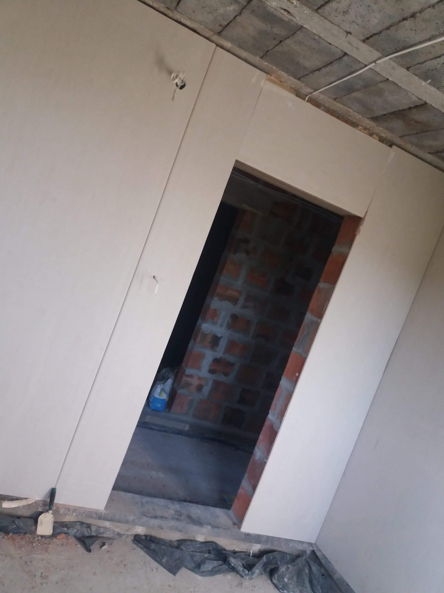 Montaż płyty karton gips wokół otworu drzwiowego, widoczne fragmenty muru i niedokończone wykończenie sufitu.