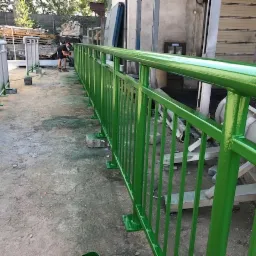 Malowanie proszkowe zielonej metalowej balustrady na zewnątrz, widoczny pracownik w tle podczas aplikacji farby.