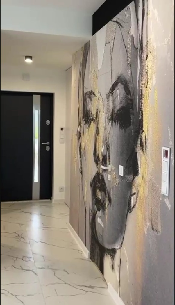 Korytarz z marmurową podłogą i ścianą ozdobioną abstrakcyjnym portretem kobiety w odcieniach szarości i złota.