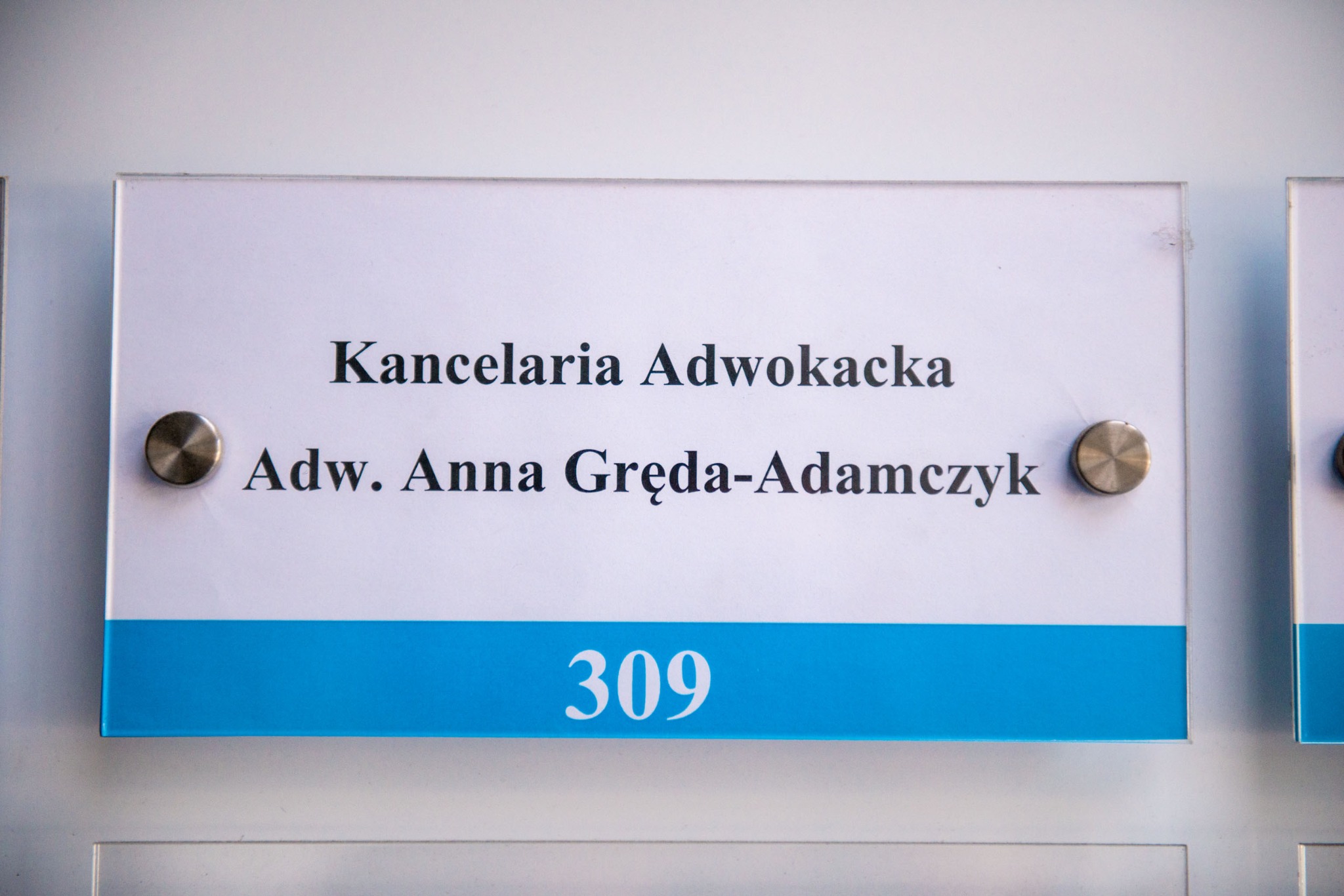Tabliczka informacyjna z napisem 'Kancelaria Adwokacka, Adw. Anna Gręda-Adamczyk' i numerem pokoju 309, zamocowana na metalowych dystansach.