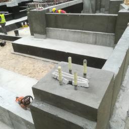 Darex firma budowlana Dariusz Jóźwiak - Wykop z betonowymi fundamentami w trakcie budowy, widoczny pracownik w żółtym kasku i odblaskowej kamizelce, narzędzia budowlane i fragment piasku.