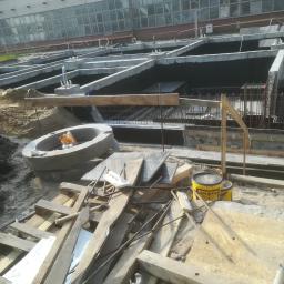 Darex firma budowlana Dariusz Jóźwiak - Budowa fundamentów: Wykop z betonowymi ścianami szalunkowymi, zbrojenie stalowe, betonowe kręgi i narzędzia budowlane na placu budowy, widok z góry.