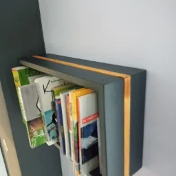 Szara, wisząca półka na książki z drewnianymi akcentami, zamontowana na ścianie w nowoczesnym wnętrzu.