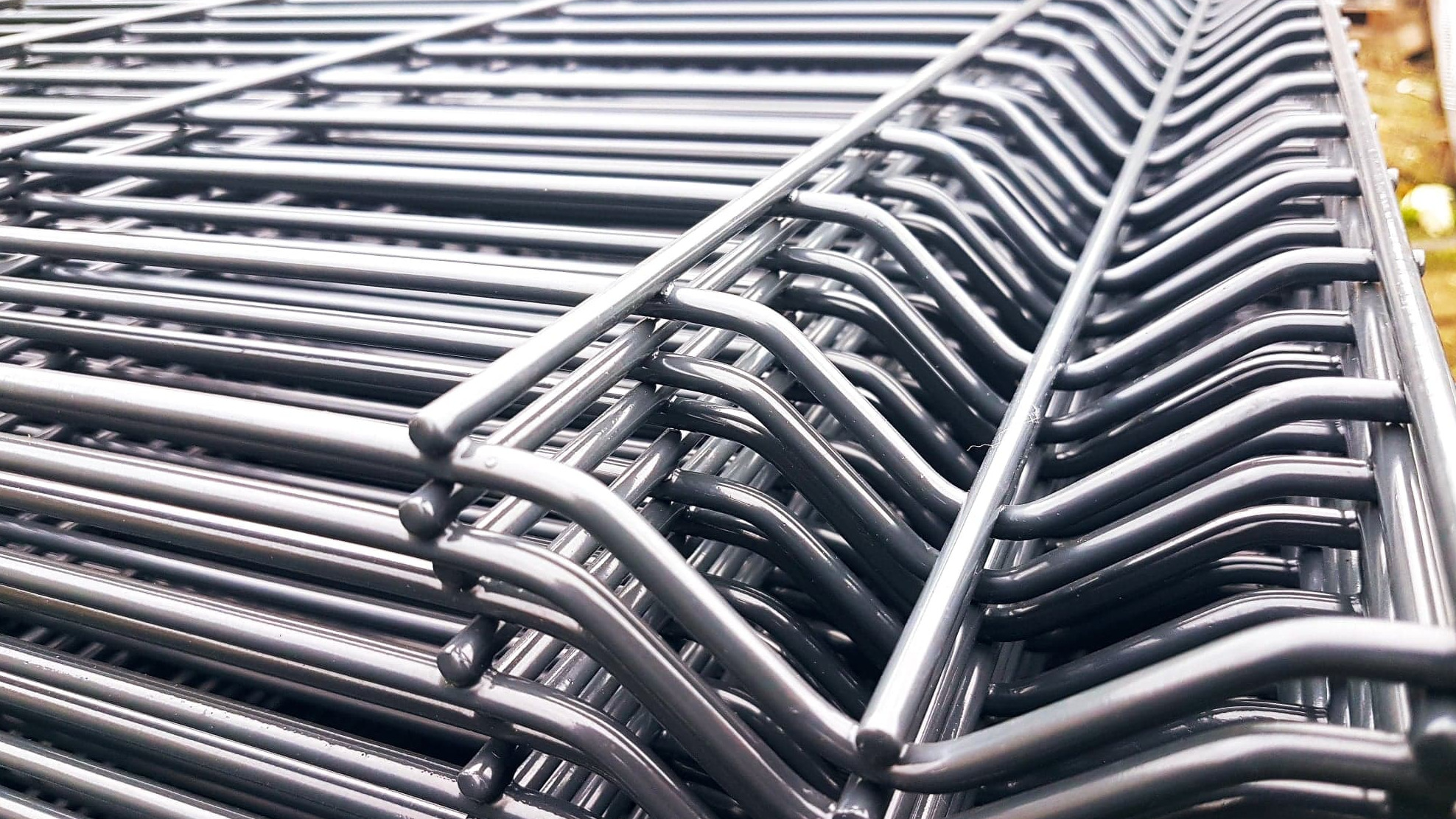 Stos paneli ogrodzeniowych z metalowego drutu, z charakterystycznymi wygięciami, przygotowanych do transportu lub montażu.