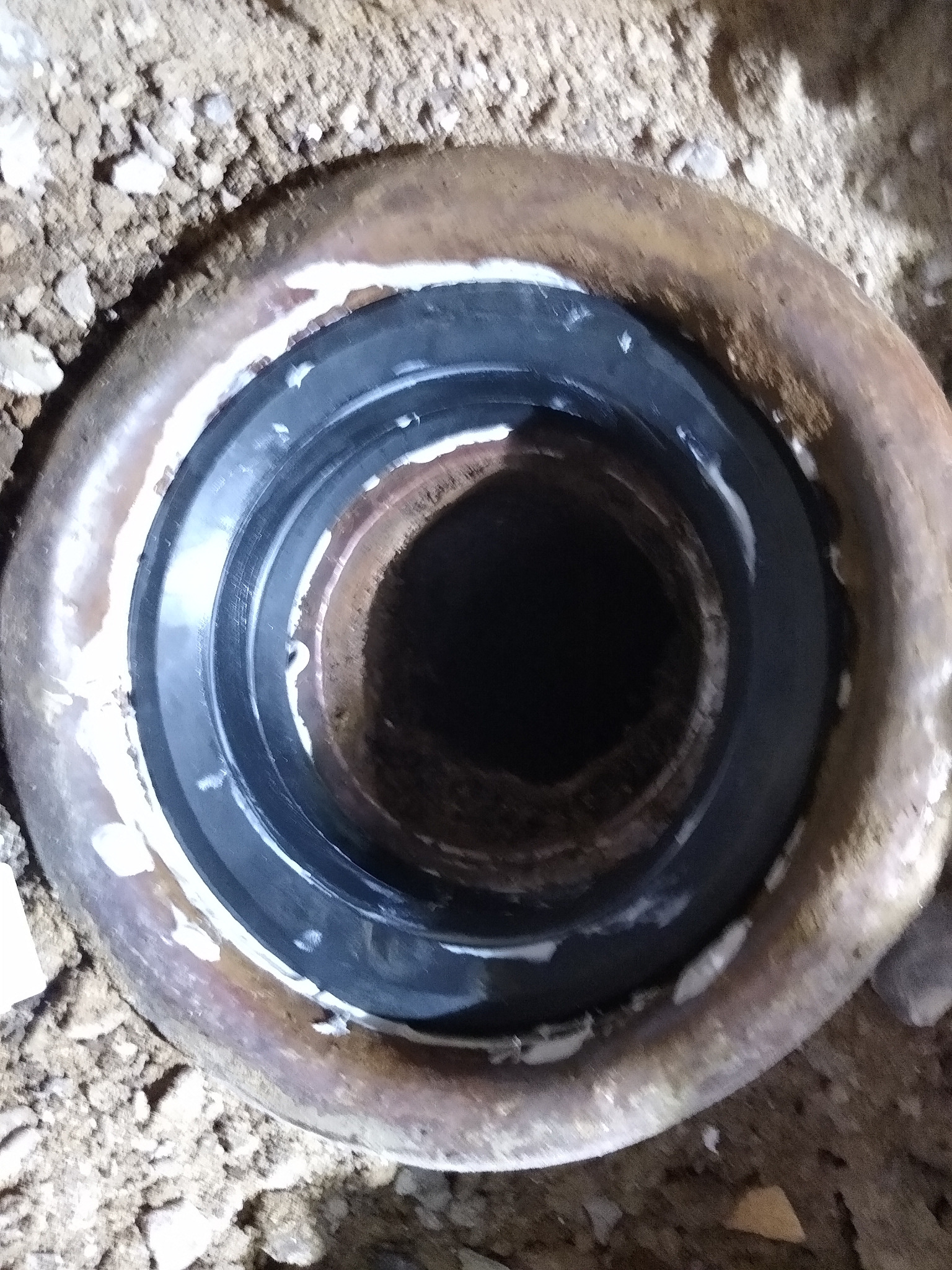 Uszczelnienie rury kanalizacyjnej z gumową uszczelką i silikonem, widok z góry, ziemiste tło.