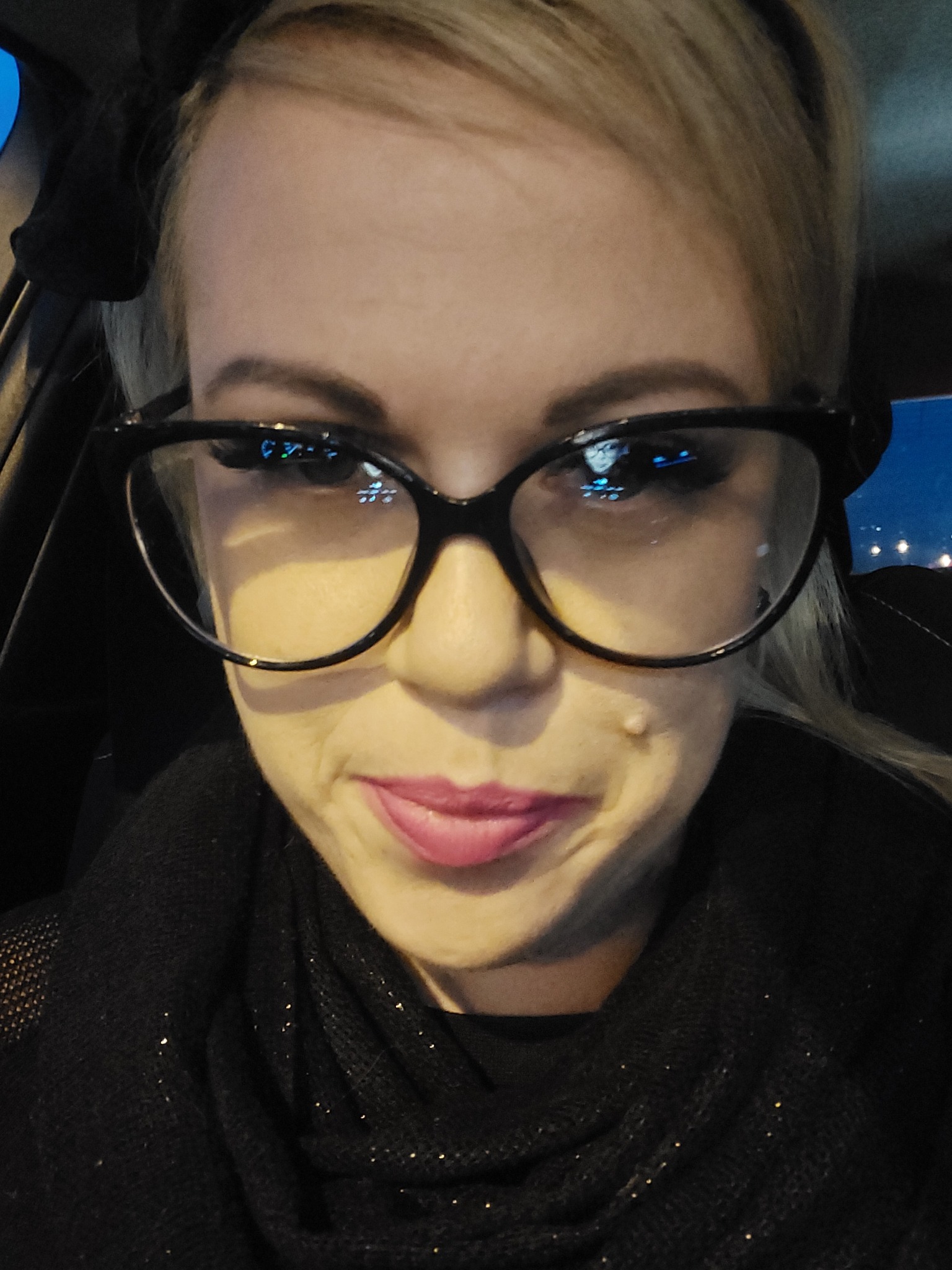 Portret kobiety w okularach w samochodzie, z odbiciem deski rozdzielczej w szkłach.