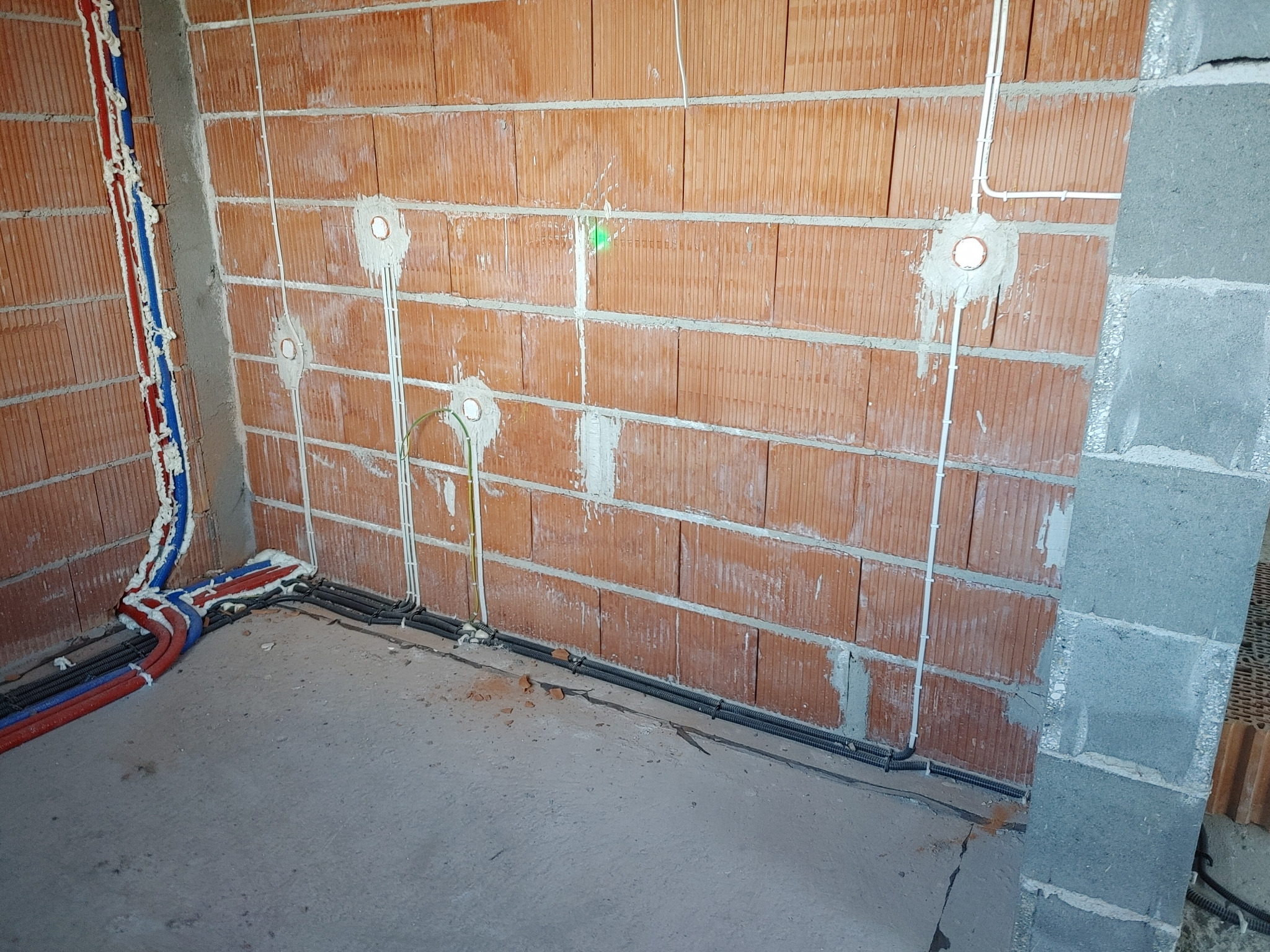 Wewnętrzne ściany z cegły dziurawki w trakcie prac instalacyjnych: widoczne peszle i przewody elektryczne oraz rury CO zabezpieczone pianką montażową.