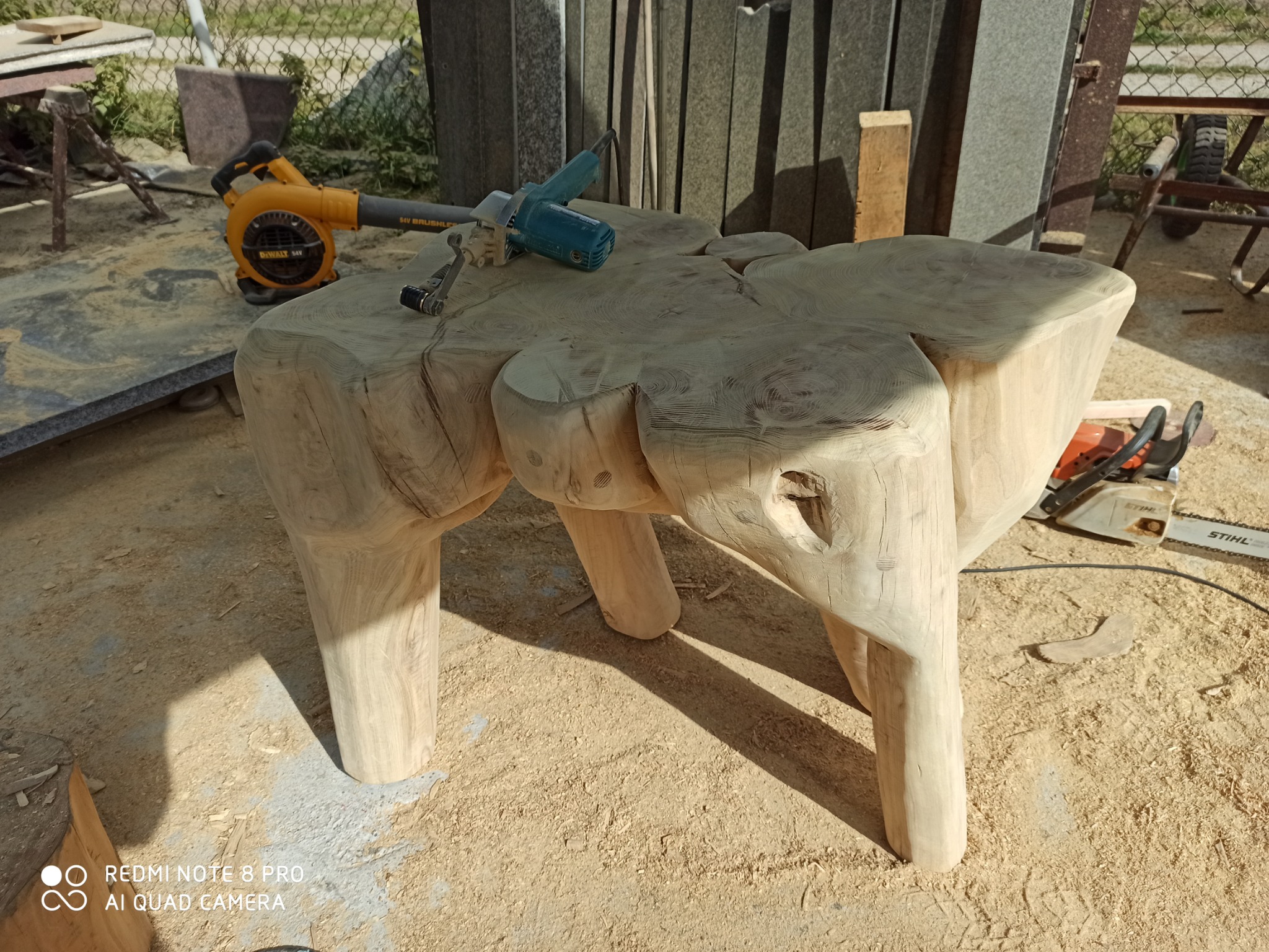 Stolik kawowy wykonany z jednego kawałka drewna, z widocznymi słojami i narzędziami do obróbki drewna w tle.