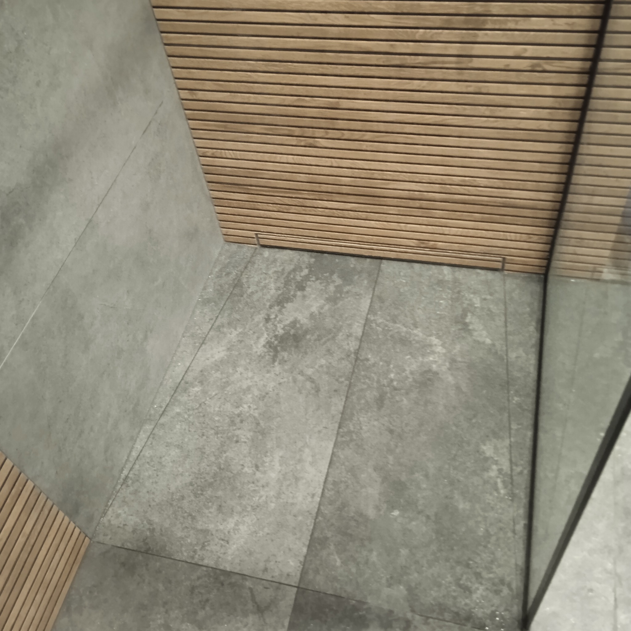 Szara, betonowa podłoga i ściany w kabinie prysznicowej z drewnianym panelem na suficie. Minimalistyczny design.