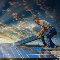 Instalator w Gdańsku montuje panel słoneczny na dachu z widocznymi mocowaniami, na tle dramatycznego nieba z promieniami słonecznymi.