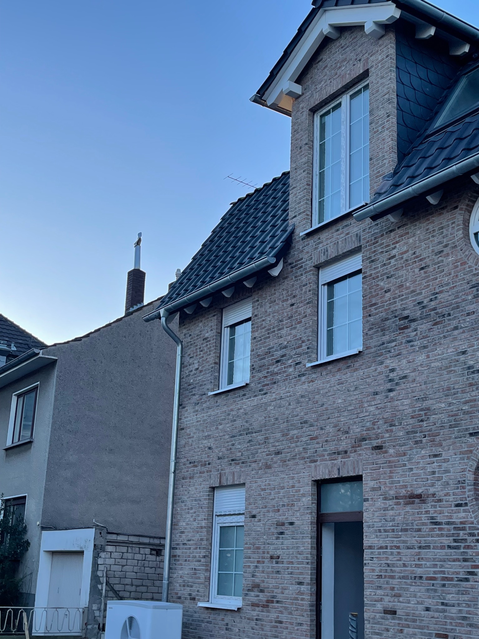 Dom z cegły klinkierowej z oknami PCV, widoczne elementy orynnowania i klimatyzator na zewnątrz.