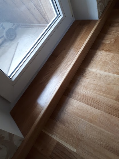 Szczegół wykończenia schodów drewnianych z dębowego parkietu, zintegrowanych z oknem, widoczne delikatne usłojenie drewna i lakierowany połysk.