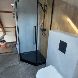 Almar Mariusz Sadczuk - Nowoczesna kabina prysznicowa z czarnymi profilami i deszczownicą, obok podwieszana toaleta. Ukończona aranżacja łazienki na poddaszu z szarą marmurową podłogą.