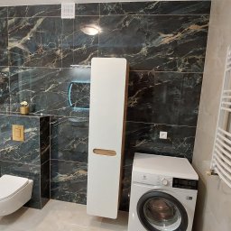 Almar Mariusz Sadczuk - Elegancka łazienka z wanną wolnostojącą, toaletą podwieszaną, szafką i pralką. Ściany wyłożone płytkami imitującymi marmur. Grzejnik drabinkowy.